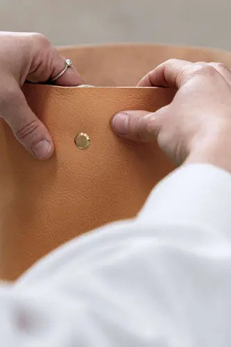 Hands inserting solid brass chicago screws into a tan coloured leather bag