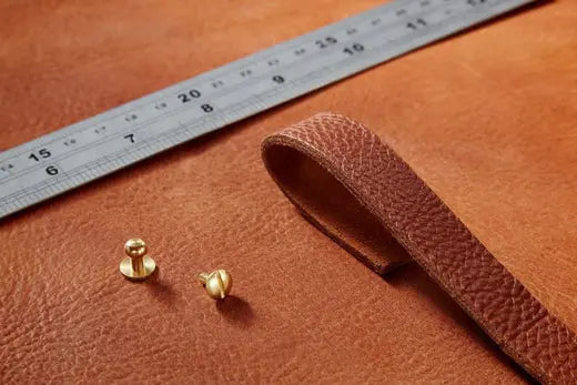 A piece of tan coloured leather with brass sam browne studs and a ruler laid on top