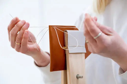 A pair of hands hand stitching leather with needles and thread