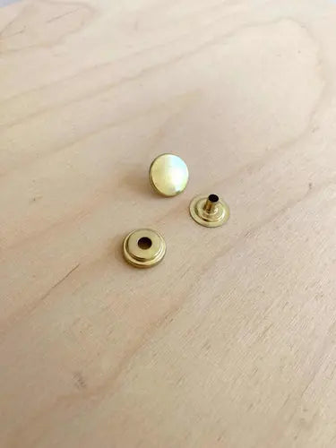 Solid brass press rivets sat on a wooden board
