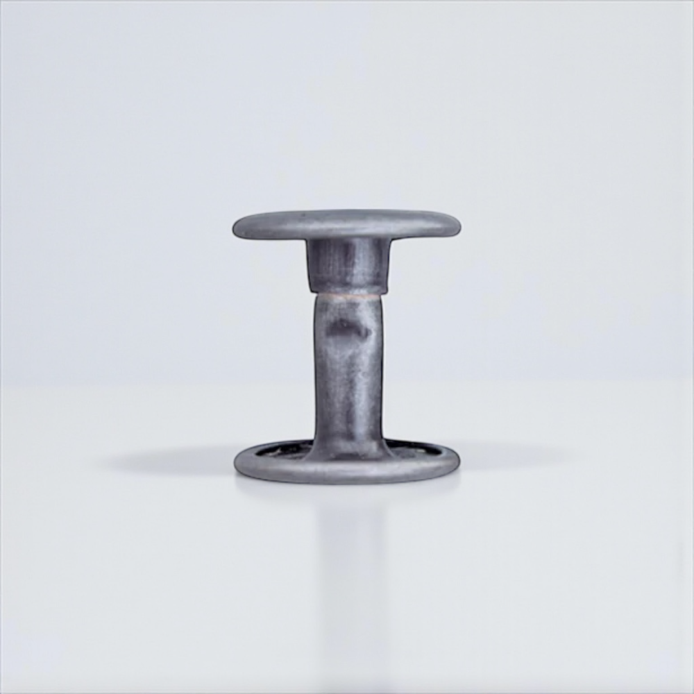 A double-cap leather rivet in matte nickel colour on a grey background