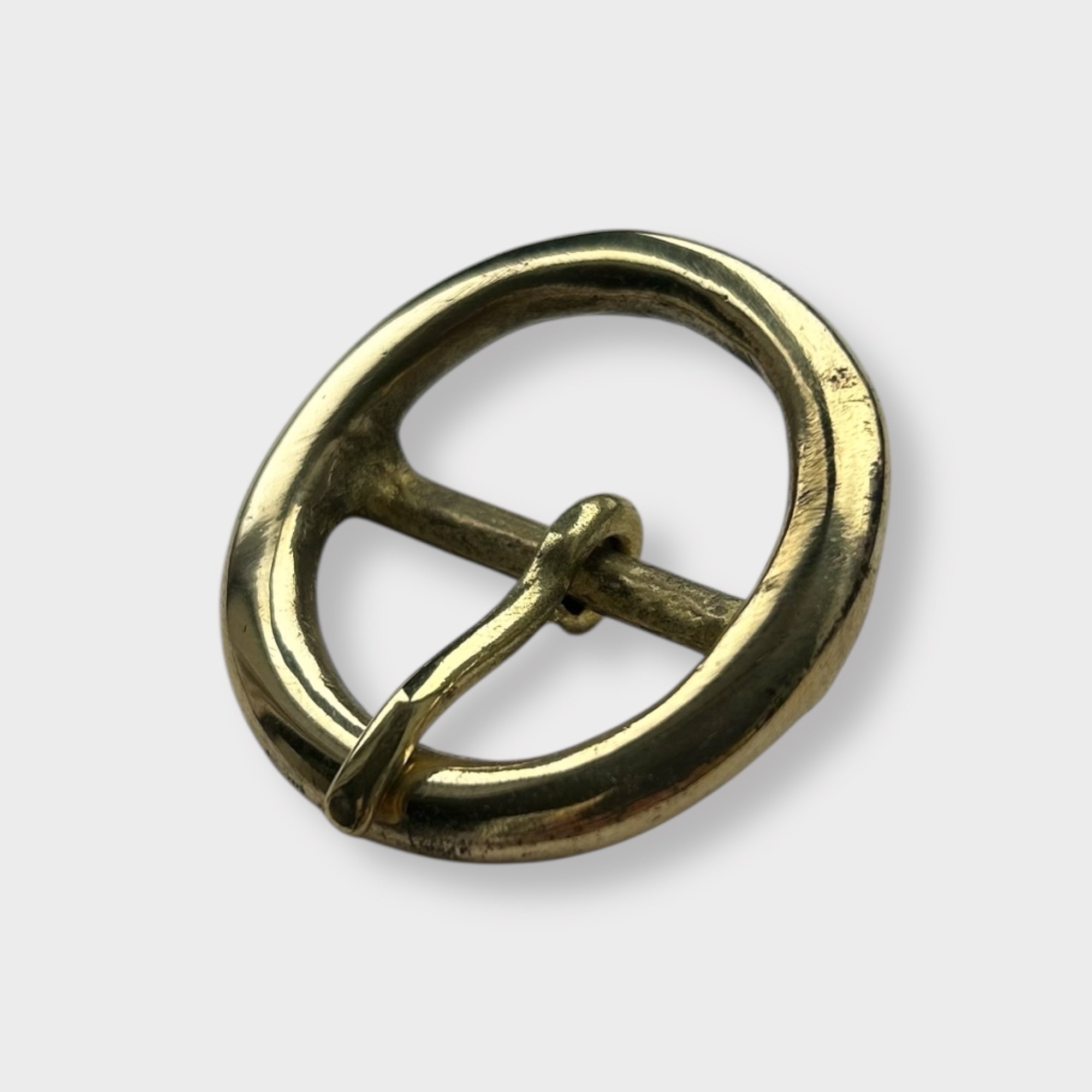 Gold coloured circular brass belt buckle on a light grey background, centre bar style.