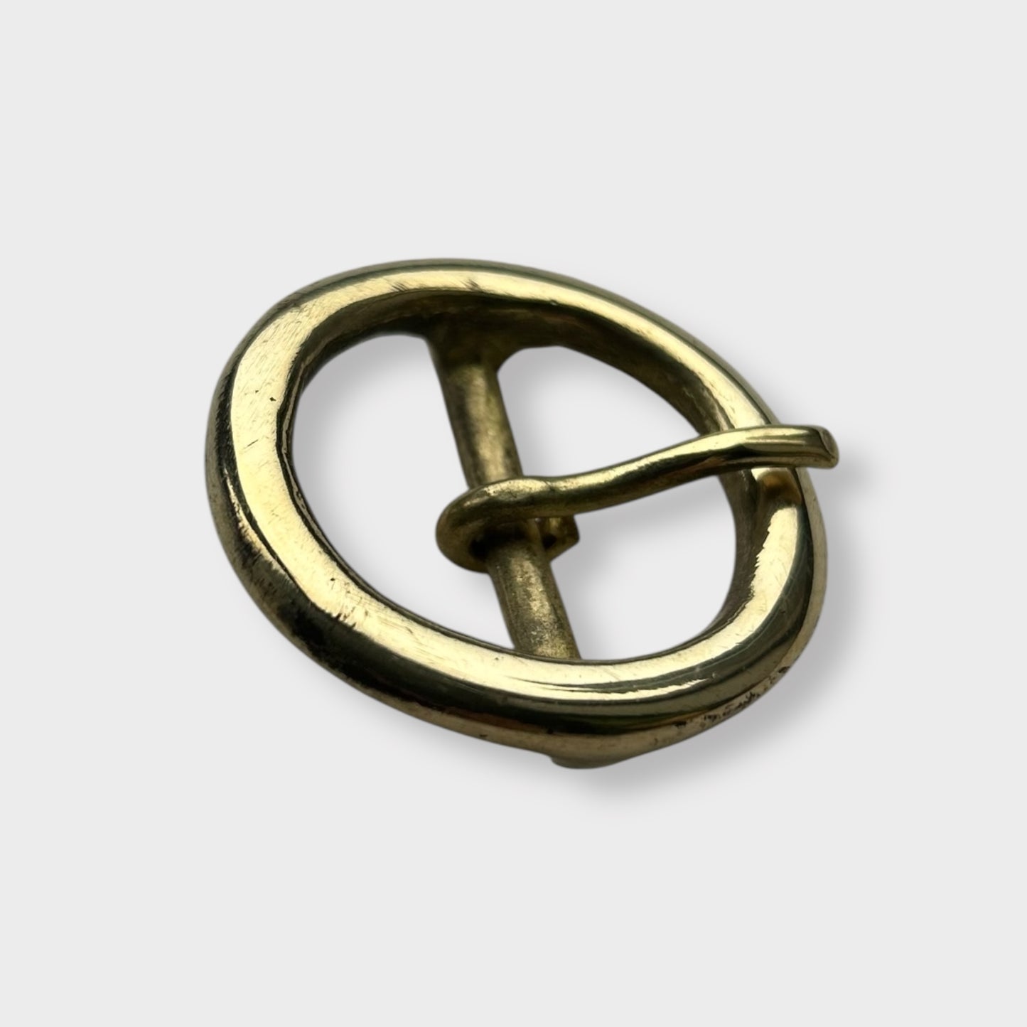 Gold coloured circular brass belt buckle on a light grey background, centre bar style.