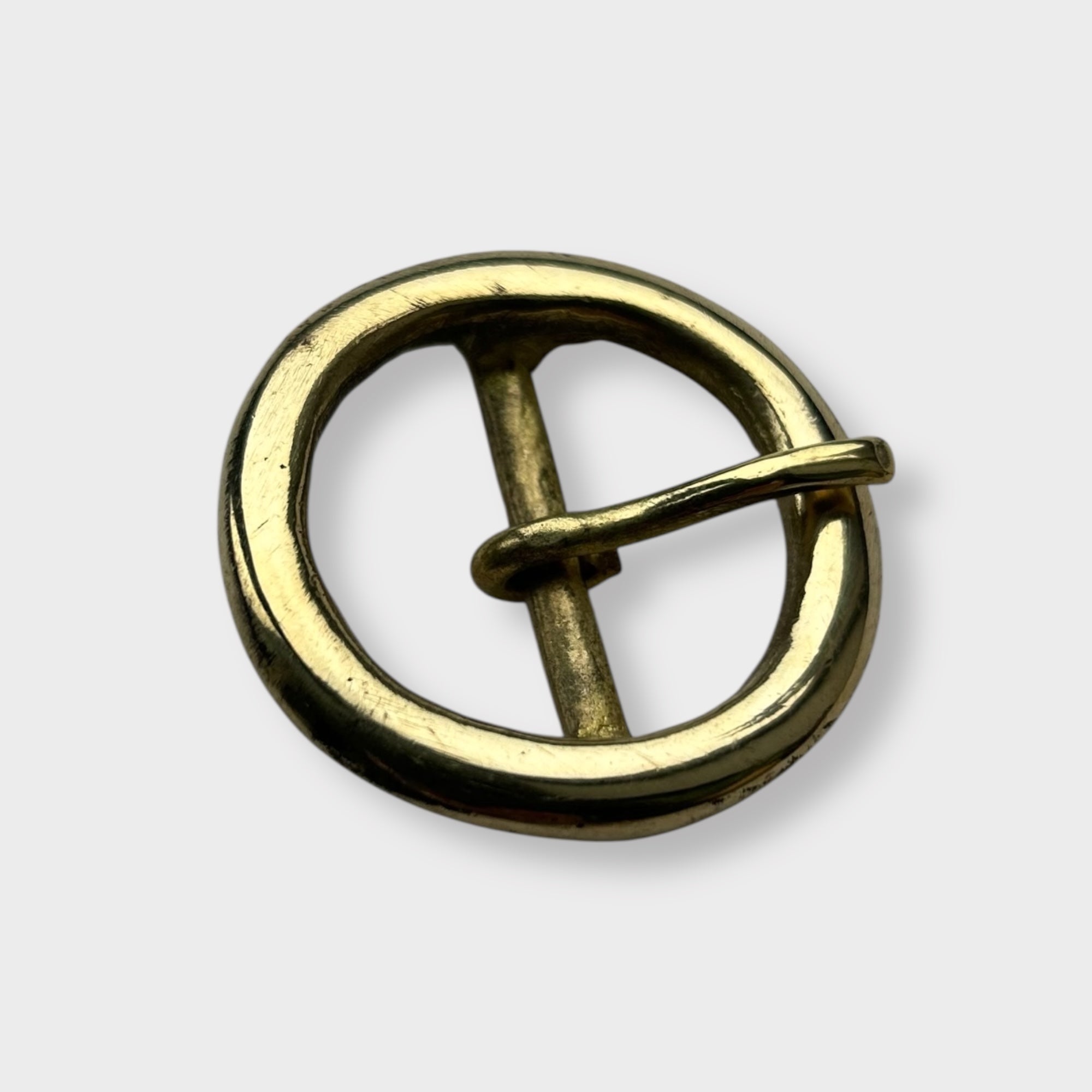 Gold coloured circular brass belt buckle on a light grey background, centre bar style.