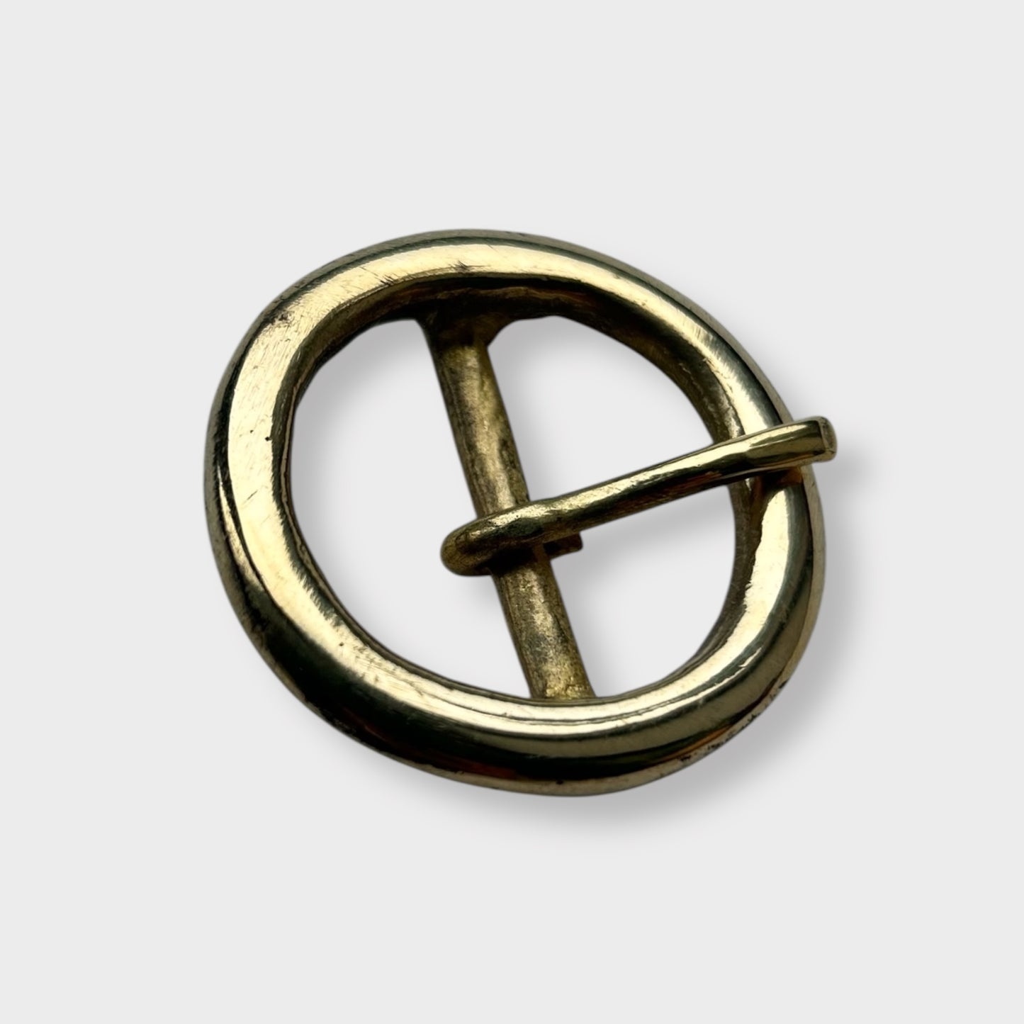 Gold coloured circular brass belt buckle on a light grey background, centre bar style.