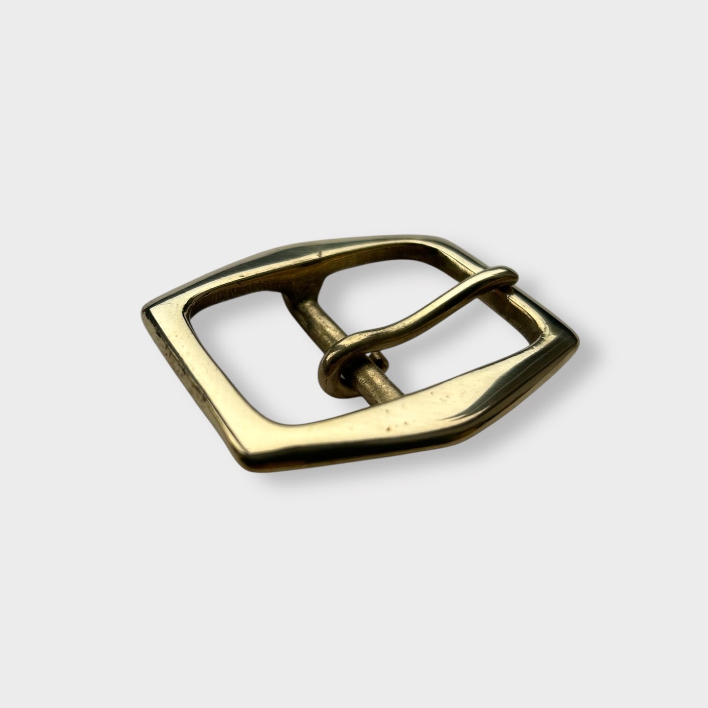Gold coloured brass belt buckle on a light grey background, centre bar style.