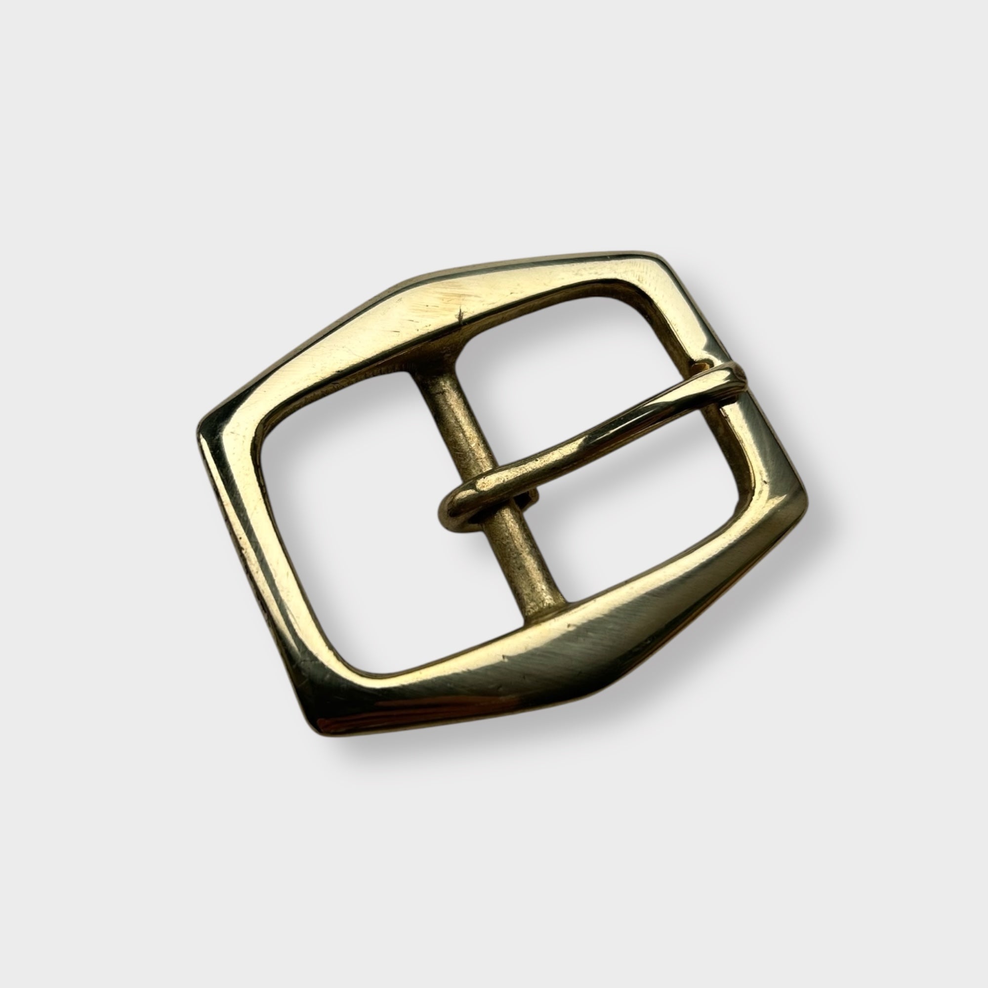 Gold coloured brass belt buckle on a light grey background, centre bar style.