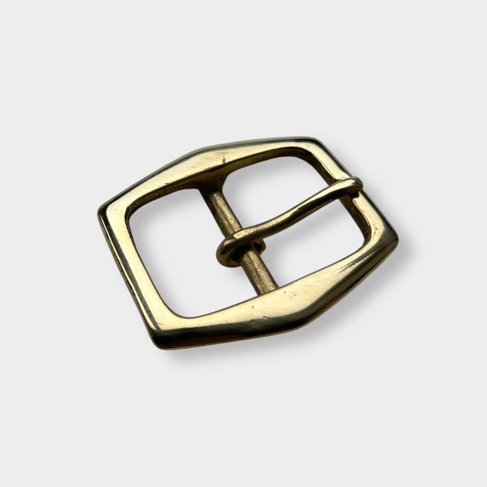 Gold coloured brass belt buckle on a light grey background, centre bar style.