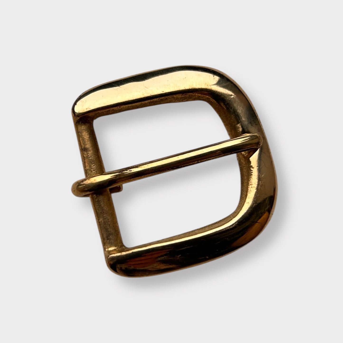 Gold coloured brass metal buckle on a light grey background.