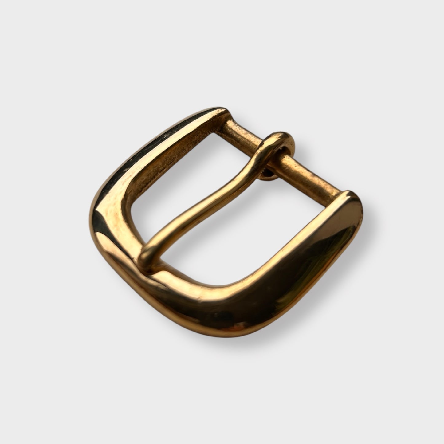 Gold coloured brass metal buckle on a light grey background.