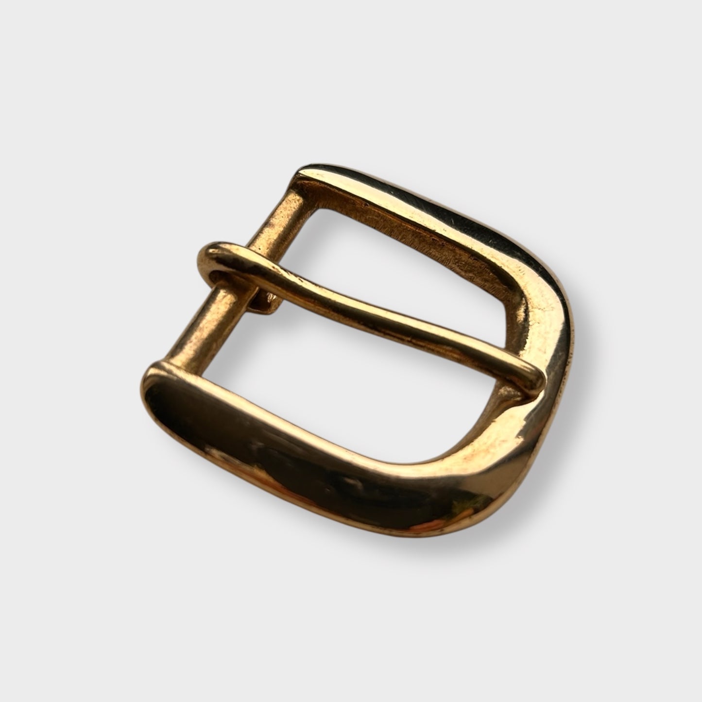 Gold coloured brass metal buckle on a light grey background.