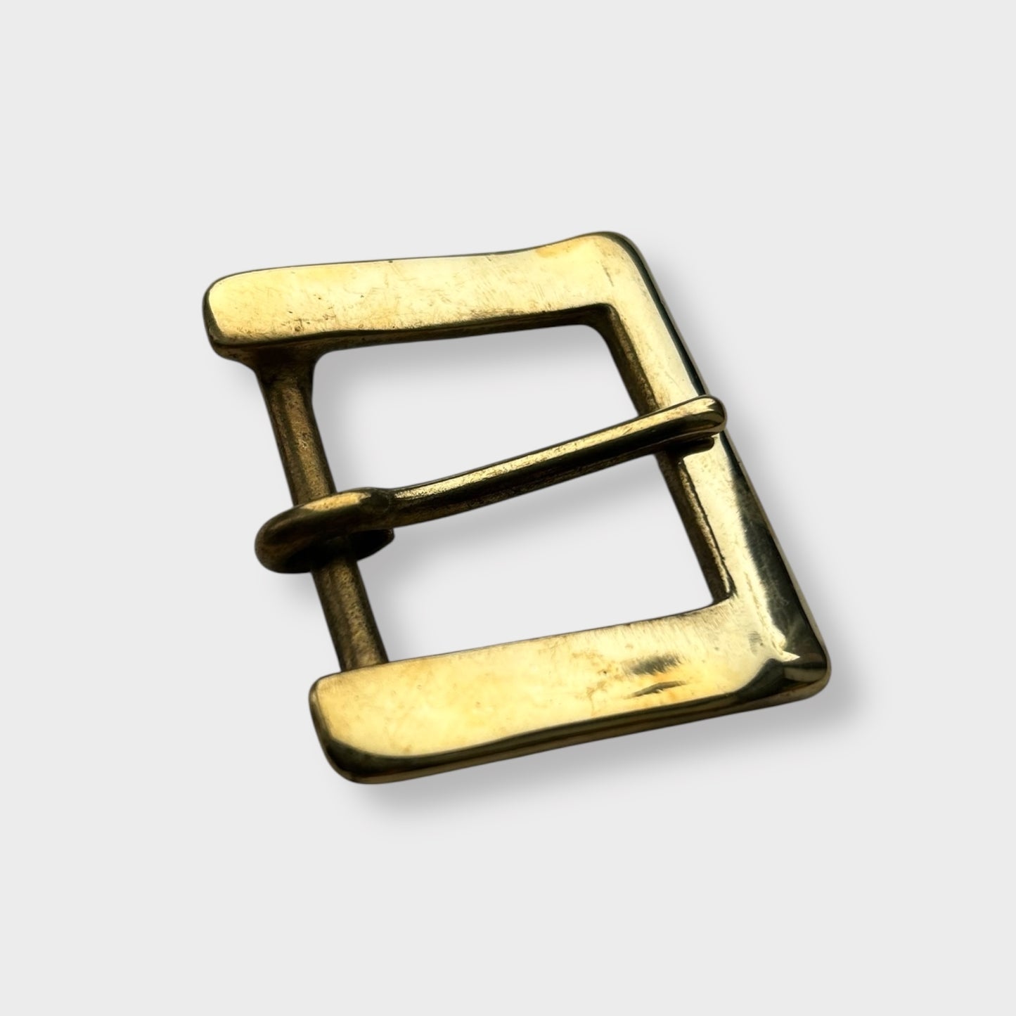 Gold coloured brass metal buckle on a light grey background.