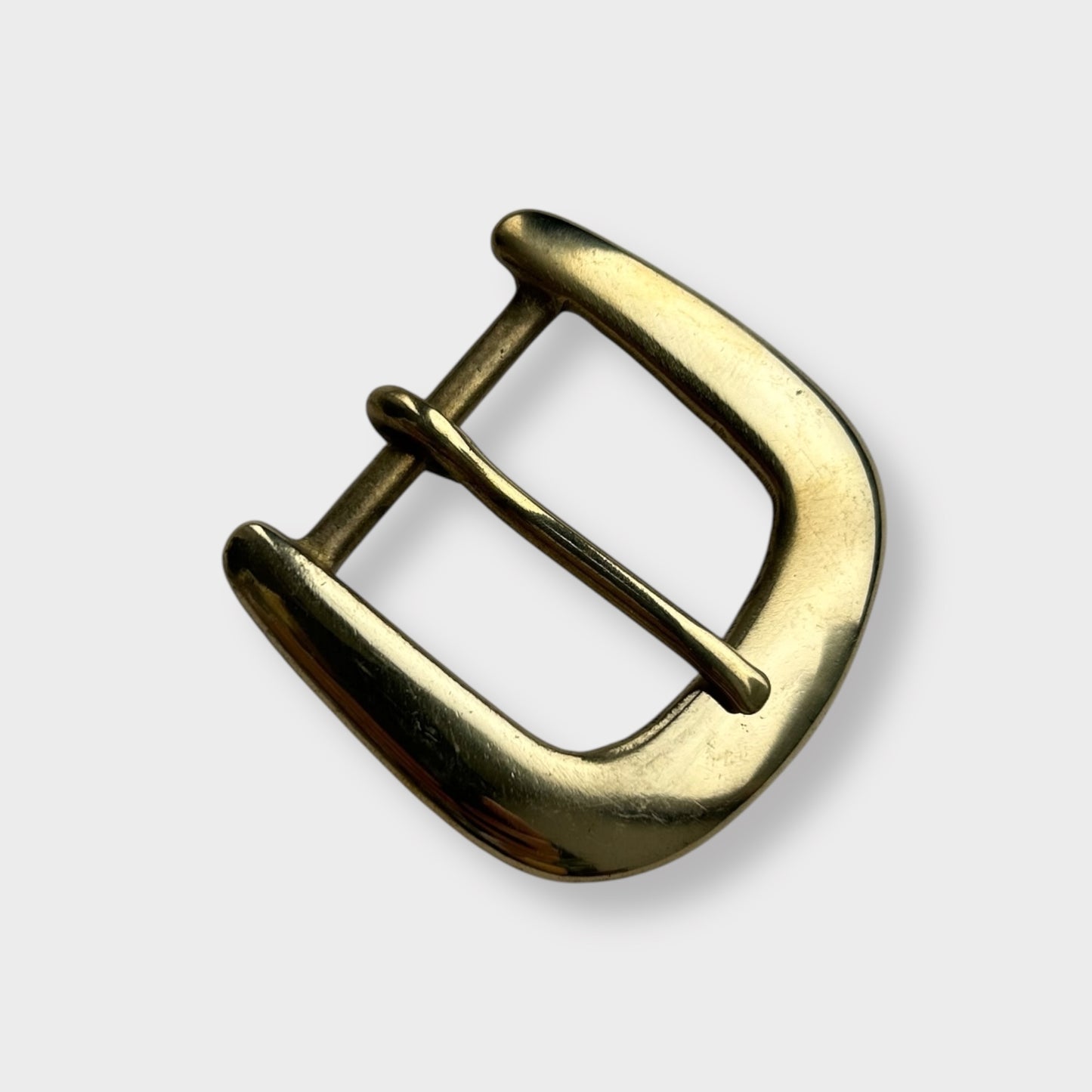Gold coloured brass metal buckle on a light grey background.