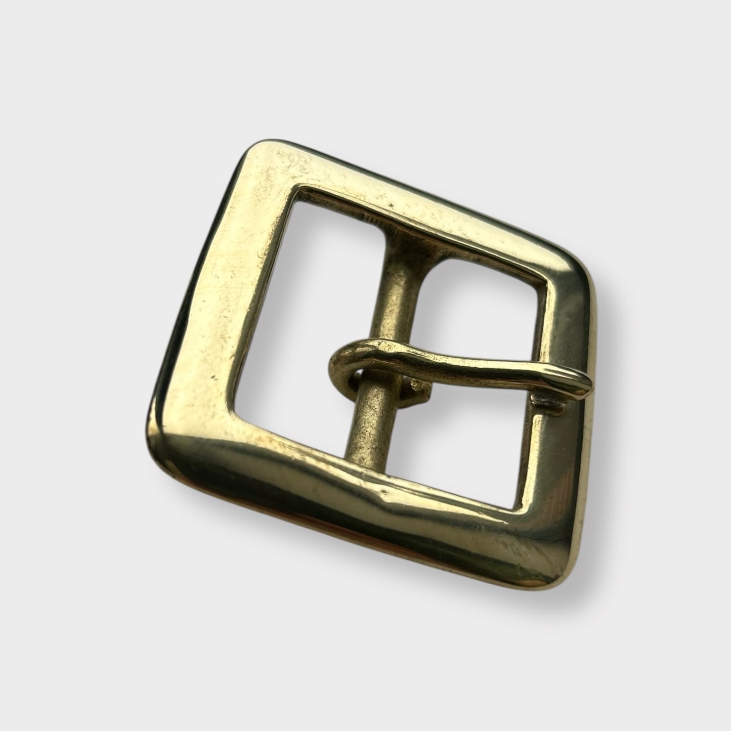 Gold coloured brass metal buckle on a light grey background.
