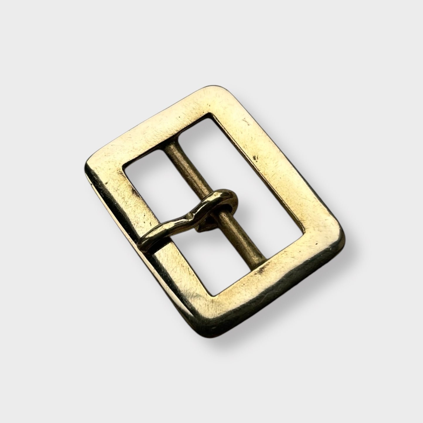 Gold coloured brass metal buckle on a light grey background.