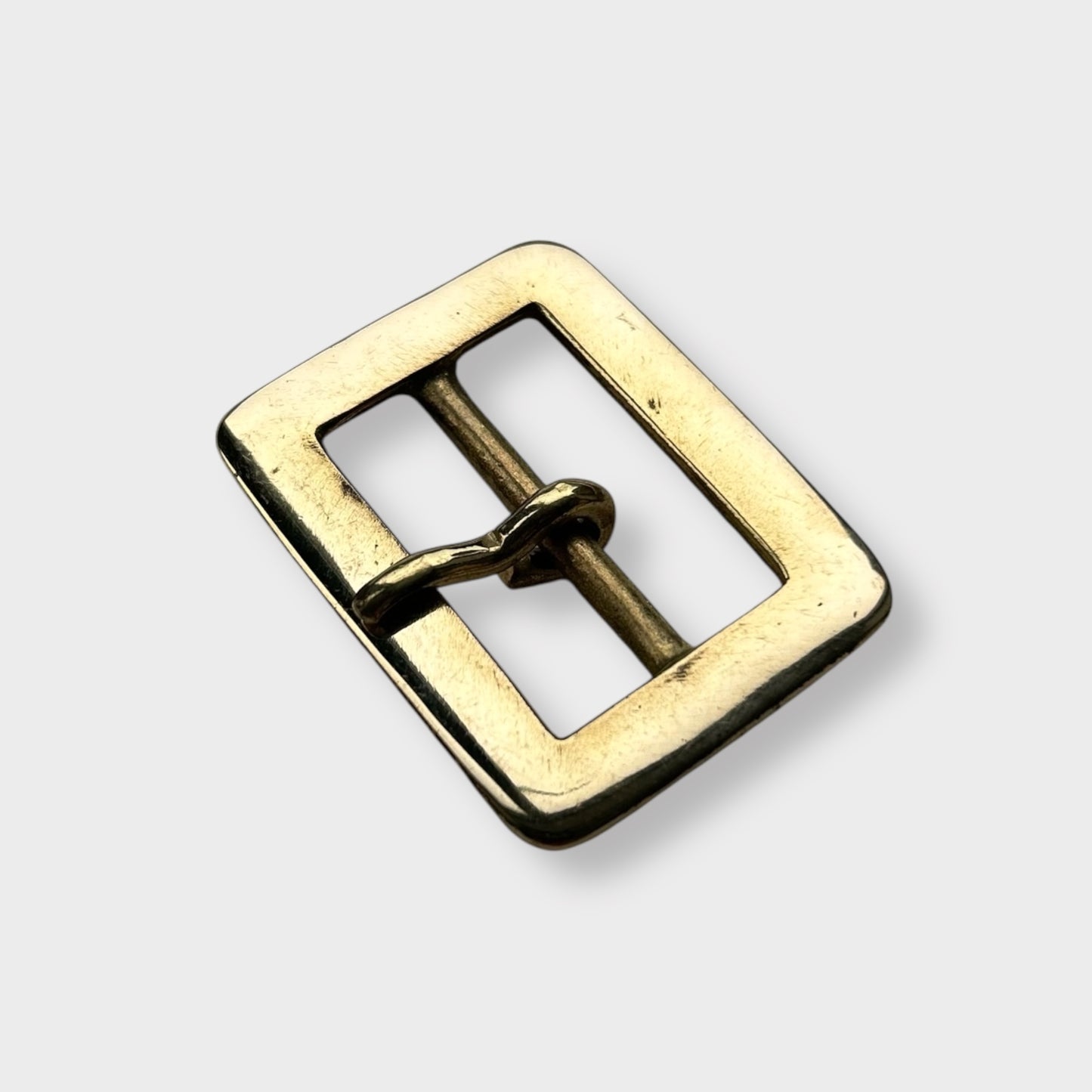 Gold coloured brass metal buckle on a light grey background.