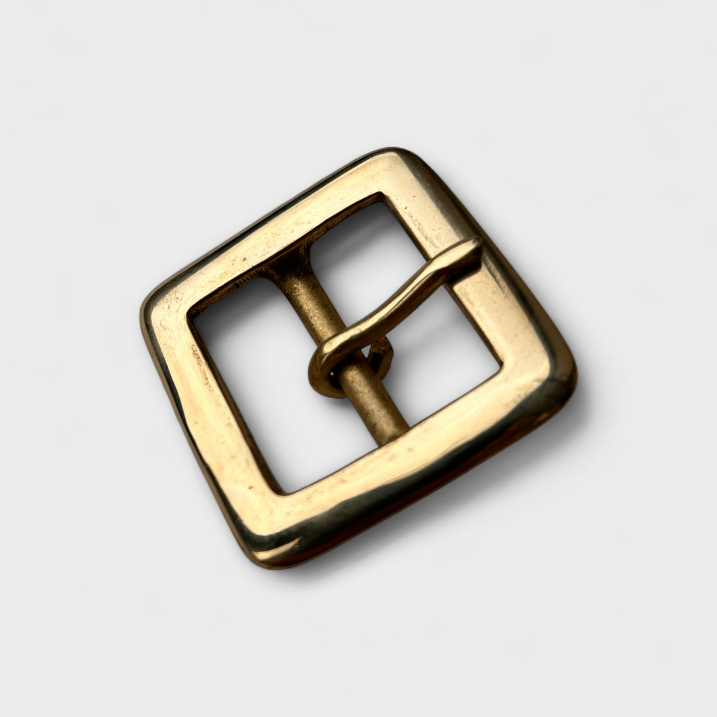 Gold coloured brass metal buckle on a light grey background.