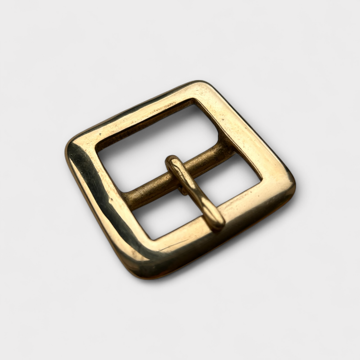 Gold coloured brass metal buckle on a light grey background.