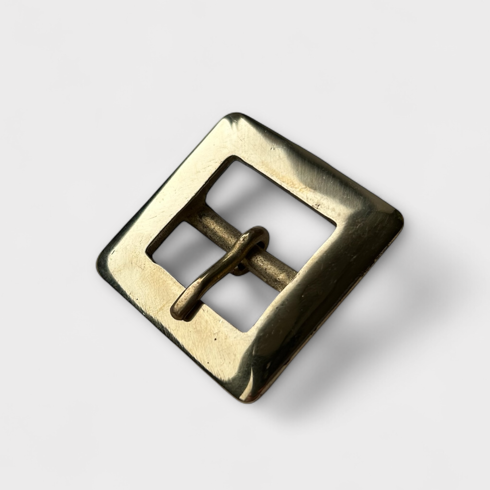 Brass-coloured square metal buckle on a light grey background
