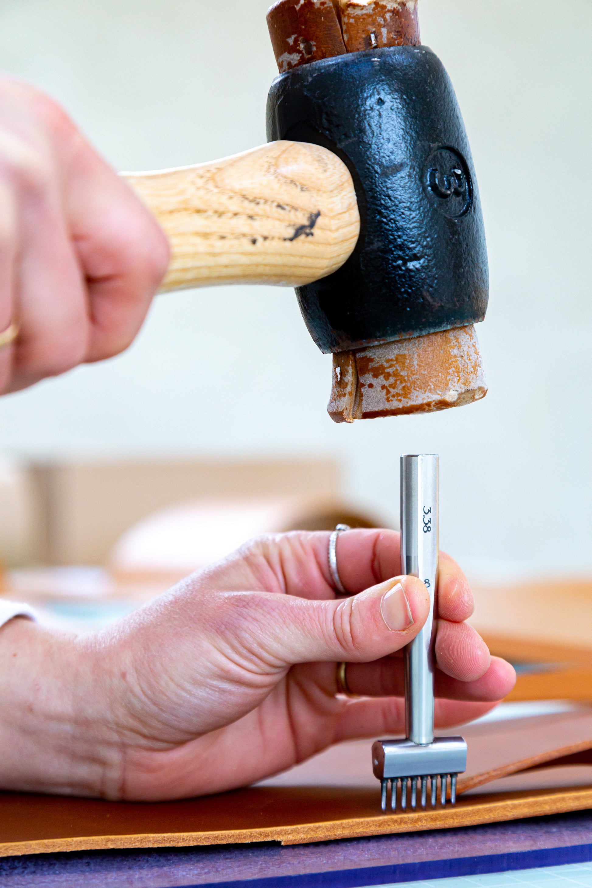 Leather worker's hands using a mallet and stitching punch