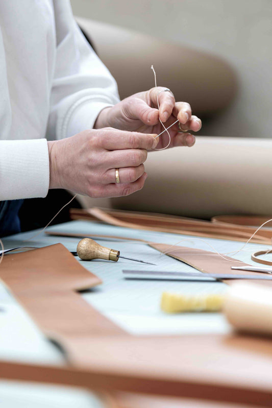 Leather worker's hands threading needles to sew leather