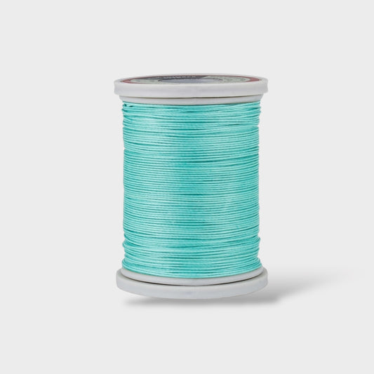 Spool of turquoise thread on a light gray background