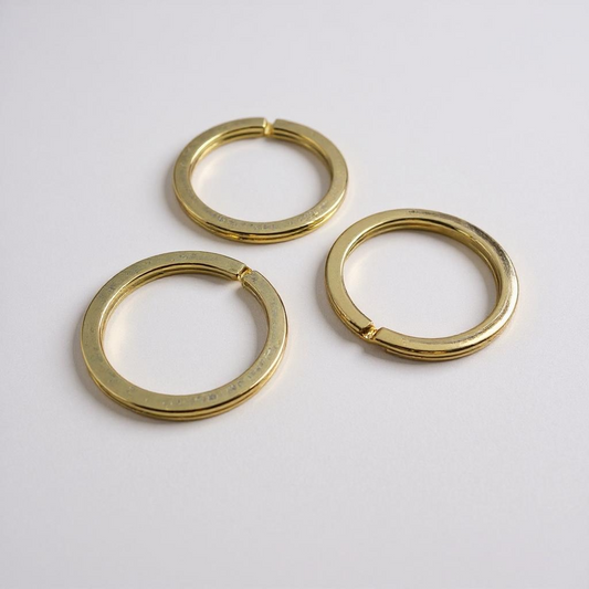 Three flat gold keyrings on a light gray background