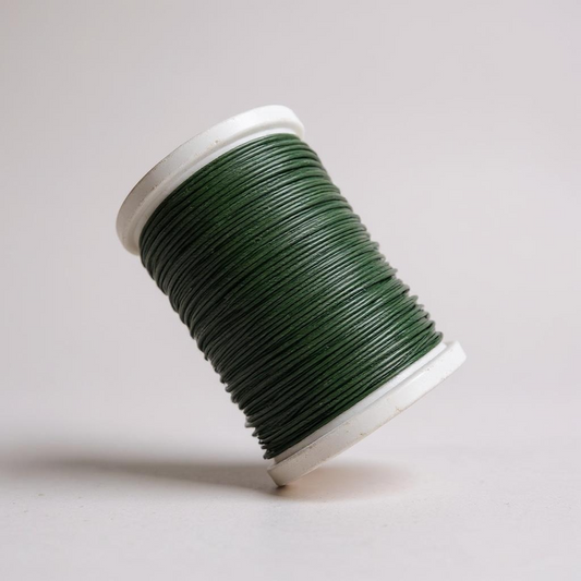 Spool of green thread for hand stitching leather on a light gray background