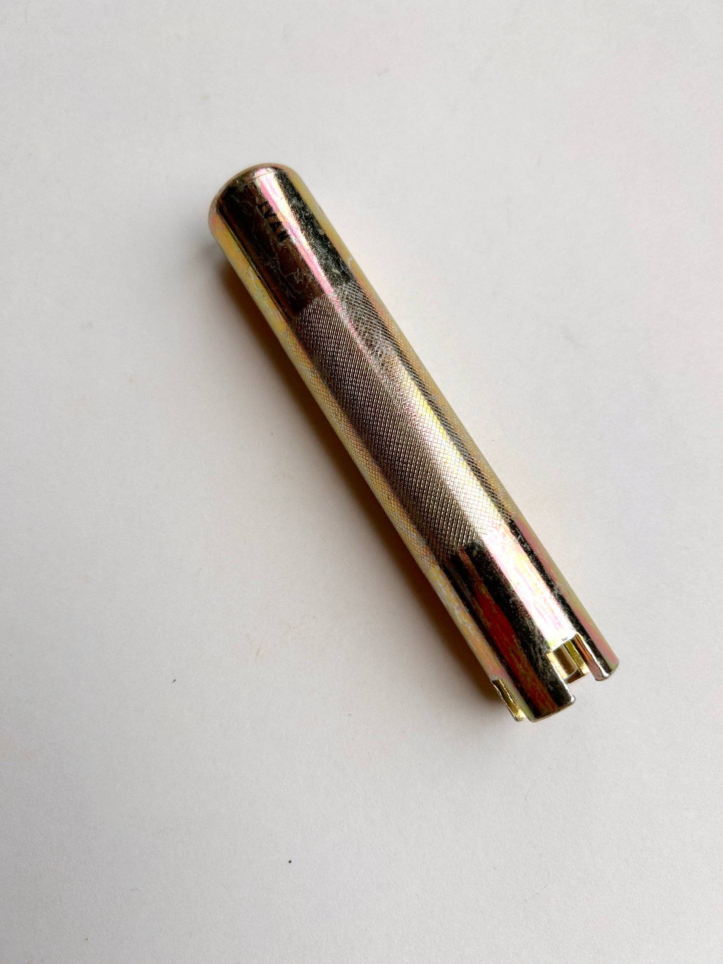 Gold-colored cylindrical metal leather embossing tool on a light grey background