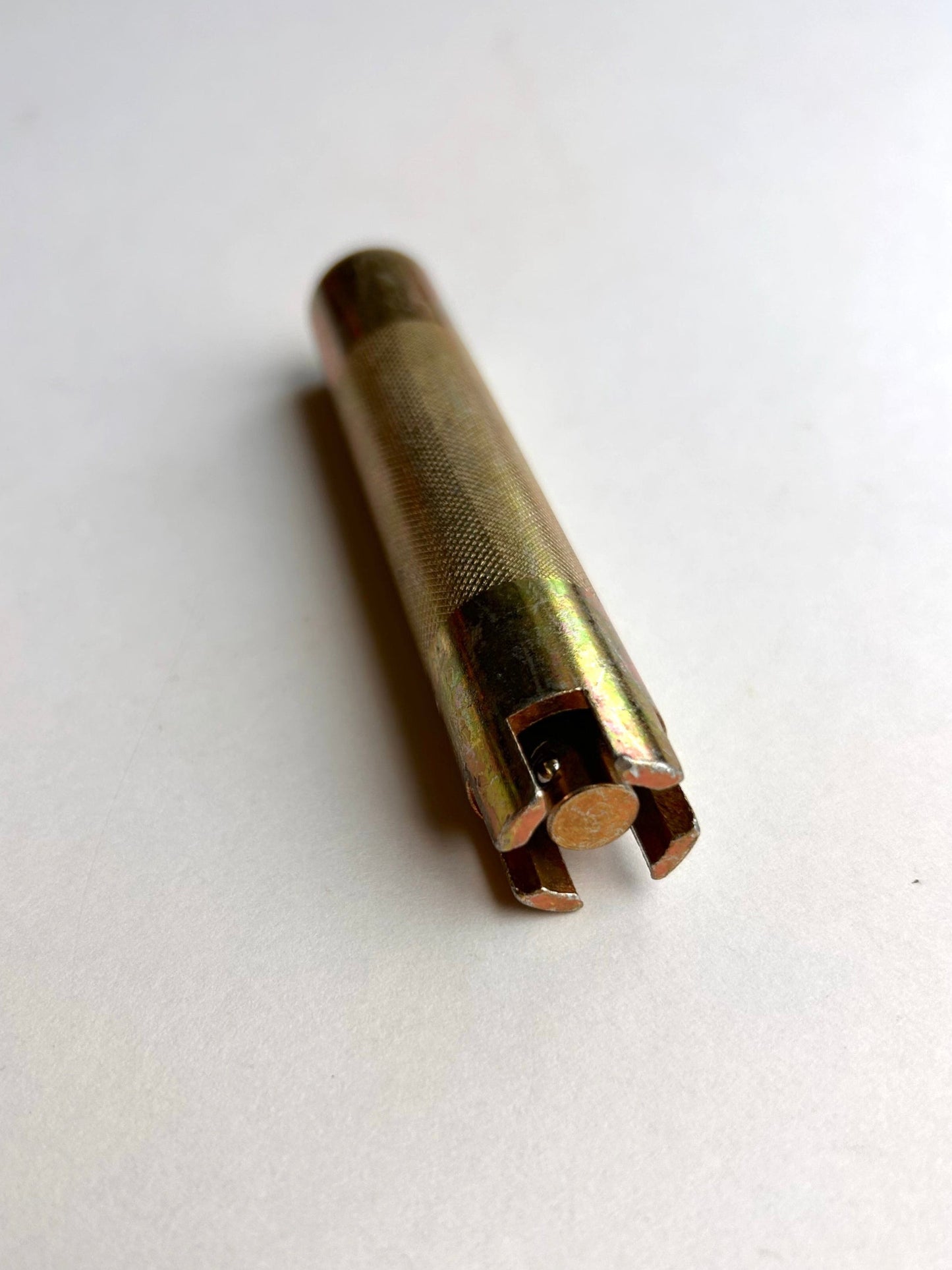 Gold-colored cylindrical metal leather embossing tool on a light grey background