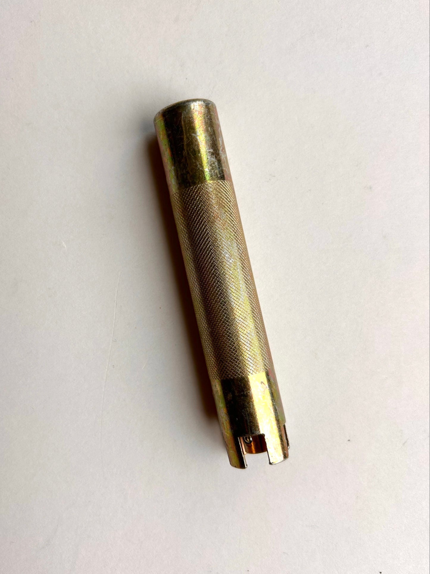 Gold-colored cylindrical metal leather embossing tool on a light grey background