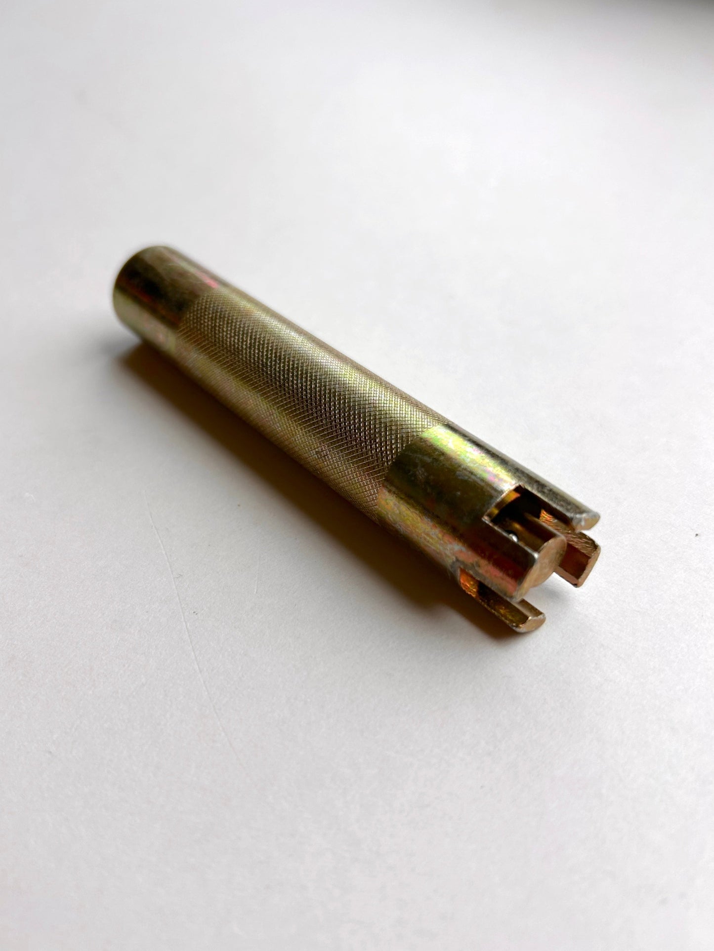 Gold-coloured cylindrical metal leather embossing tool on a light grey background