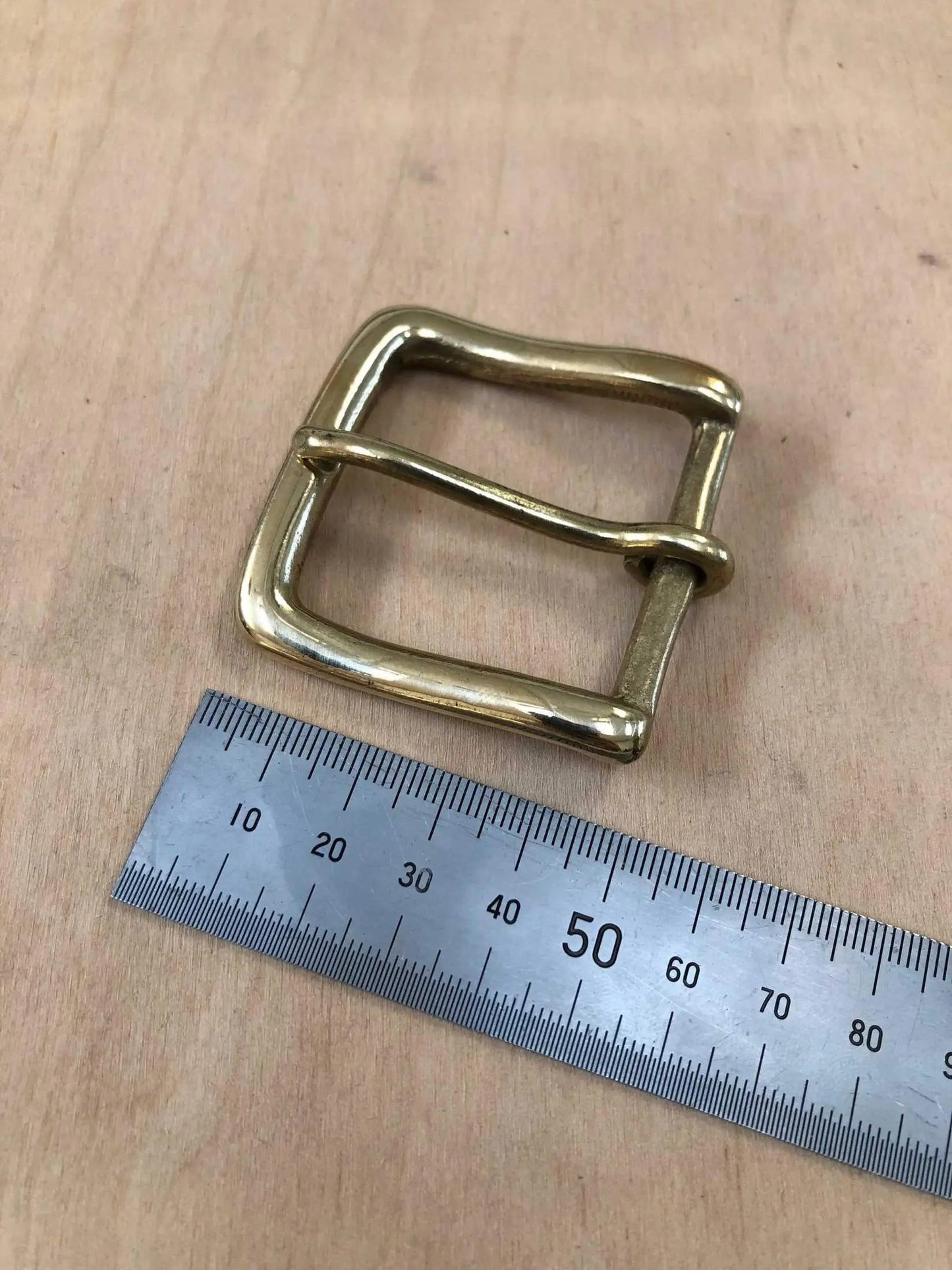 Solid brass buckle with rounded frame and pin, shown with a ruler for size reference.