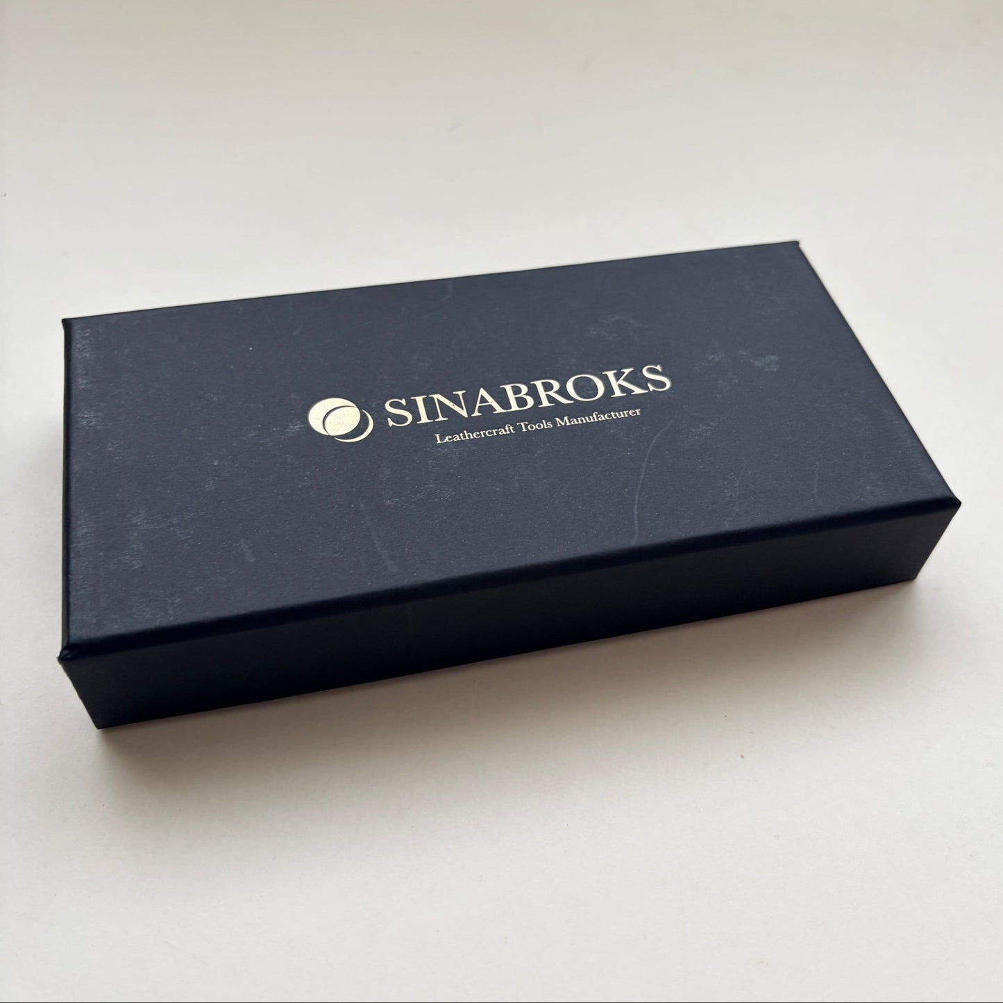 A dark navy blue rectangular box with the brand name 'SINABROKS' printed in gold on the lid, photographed on a plain off-white surface.