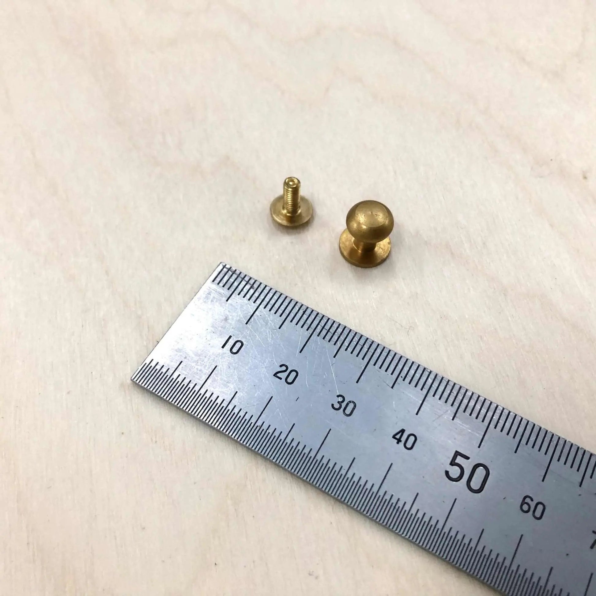 Solid brass Sam Browne Studs with screws next to a ruler for size reference.
