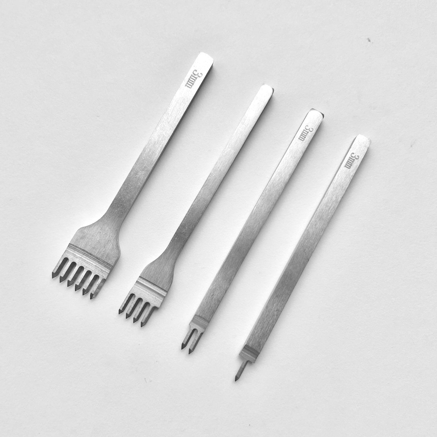 Set of four metal leather stitching punches on a light grey background