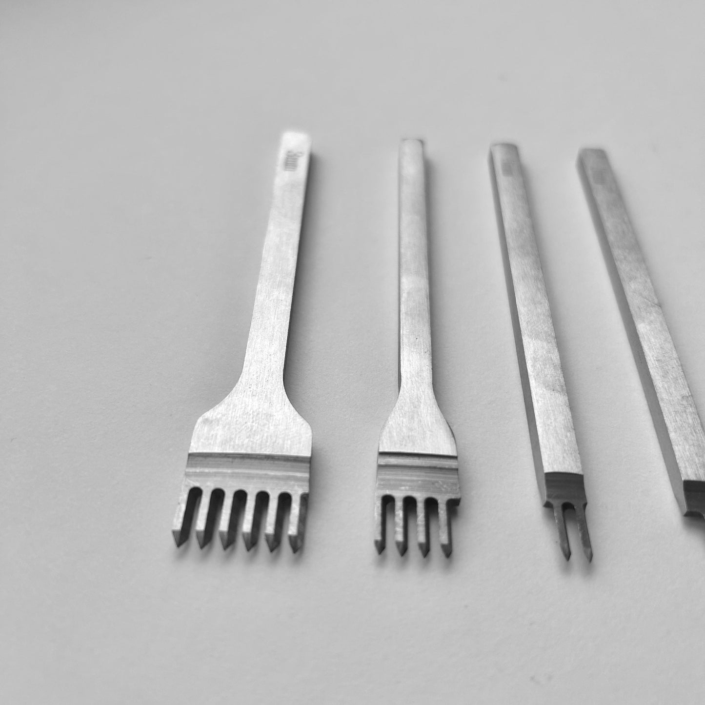 Set of four metal leather stitching punches on a light grey background
