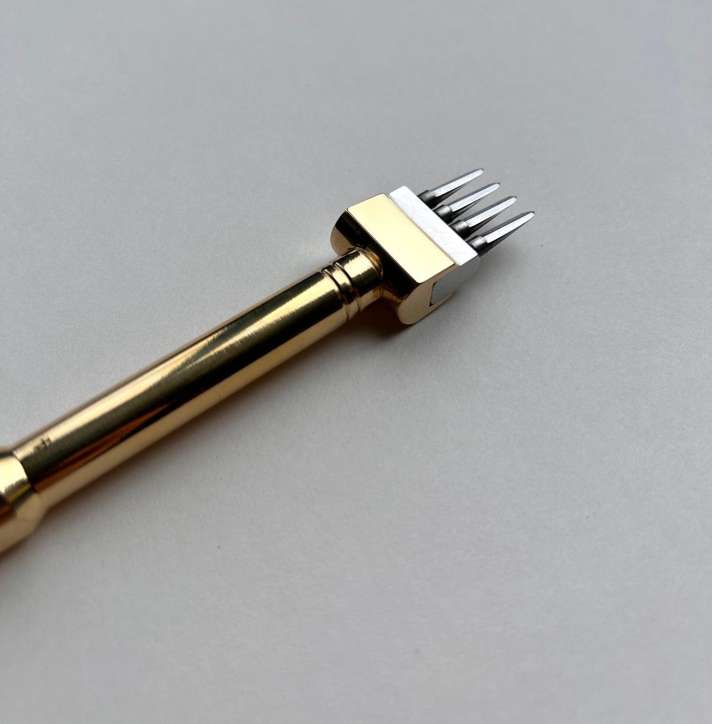 Gold-colored Sinabroks leather pricking iron tool on a light gray background