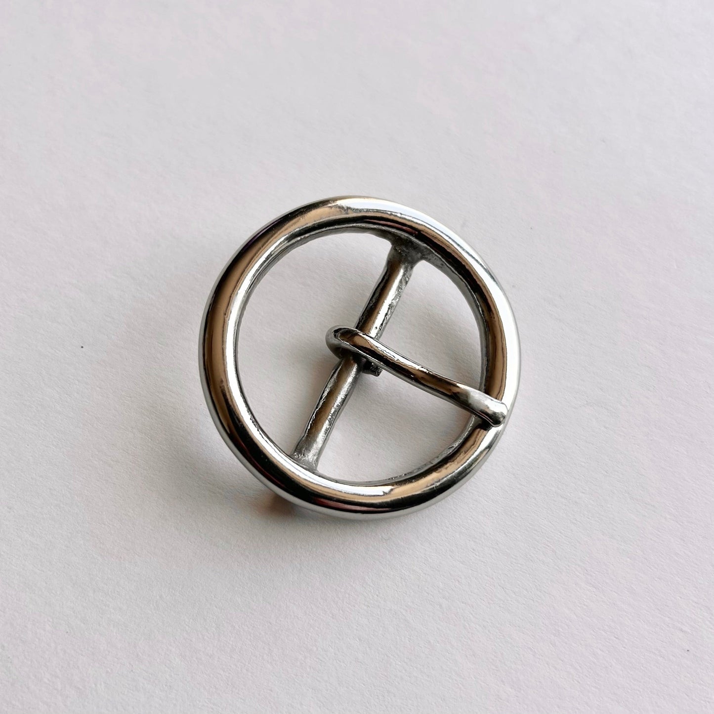 Silver metal circular buckle with a central bar on a light gray background