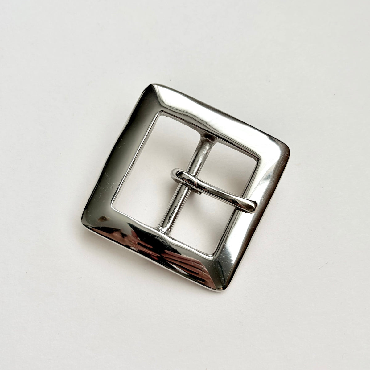 A polished silver-tone metal belt buckle with a square frame and central pin, photographed on a plain light background.