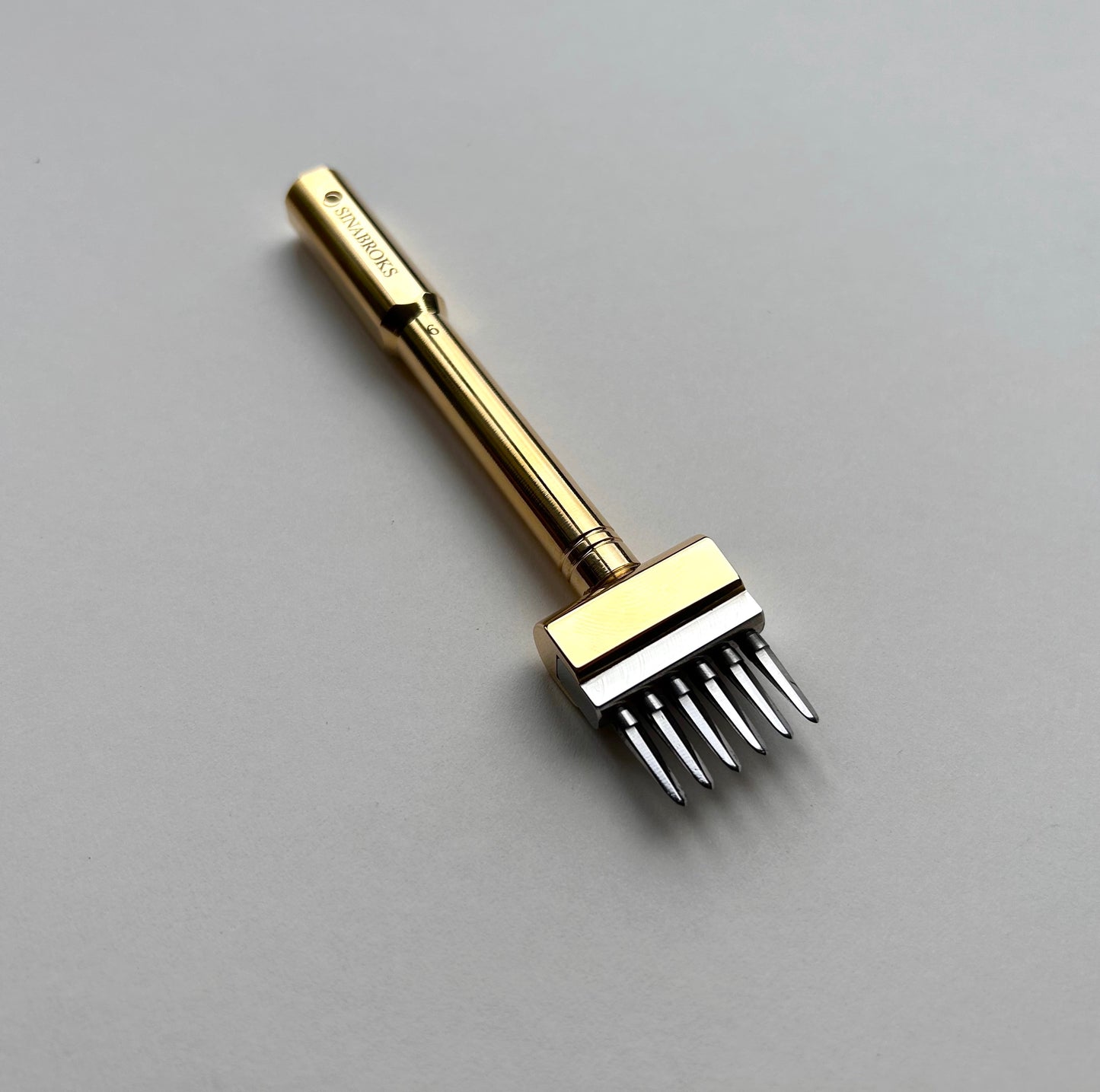Gold-colored Sinabroks leather pricking iron tool on a light gray background