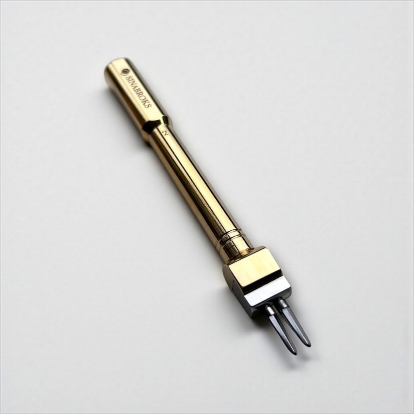 Gold-colored Sinabroks leather pricking iron tool on a light gray background