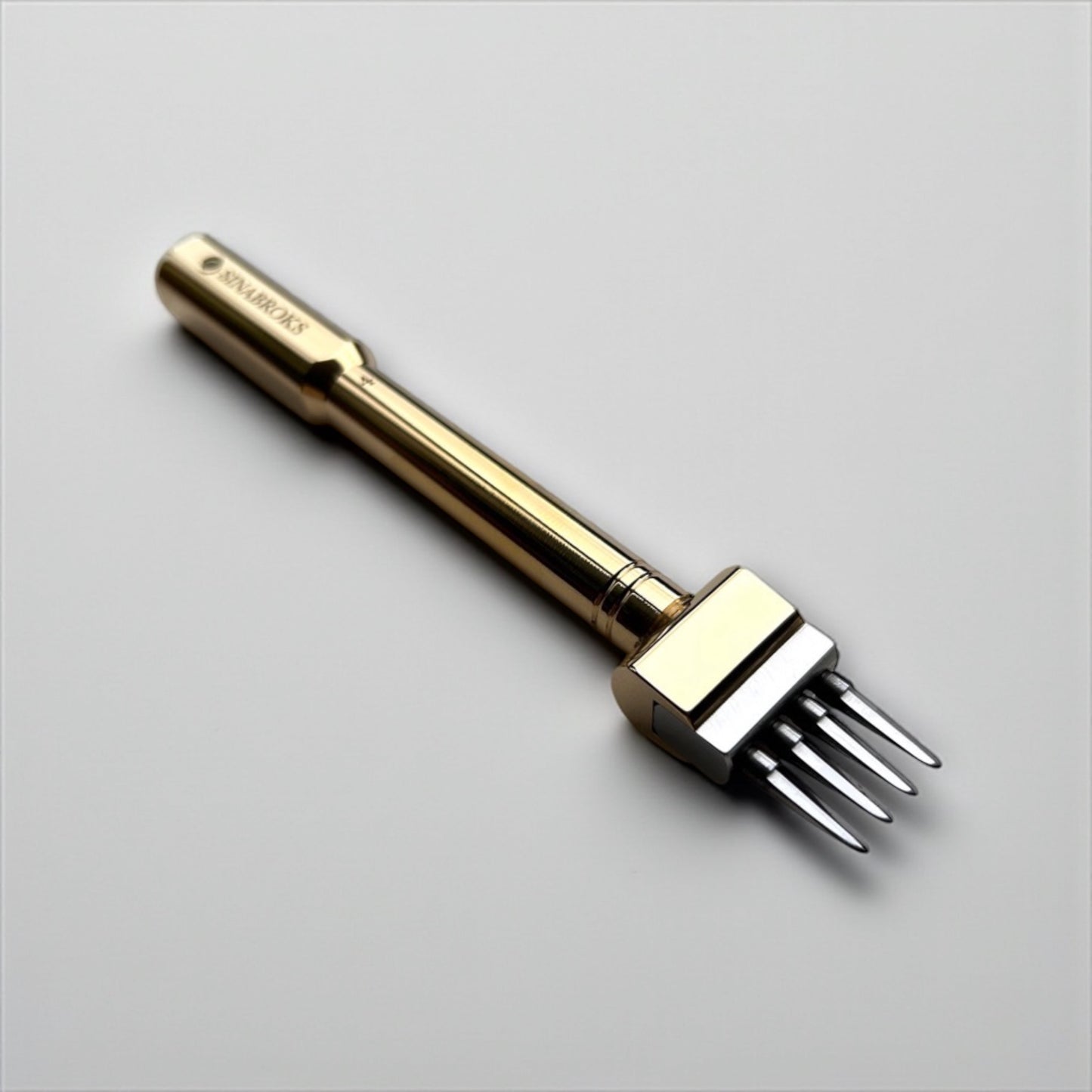 Gold-colored Sinabroks leather pricking iron tool on a light gray background