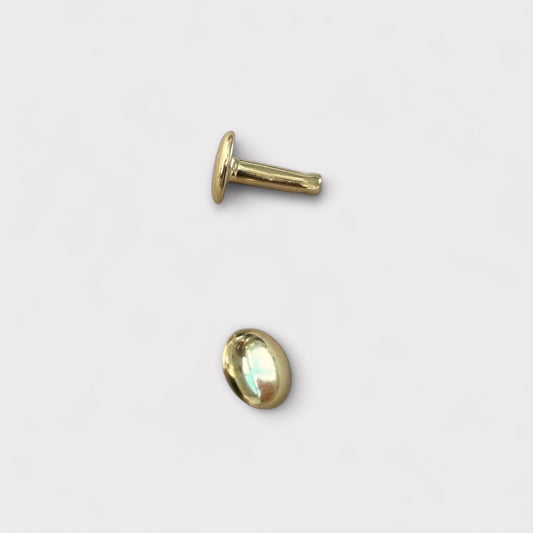 Two gold-colored brass metal leather rivets on a light grey background