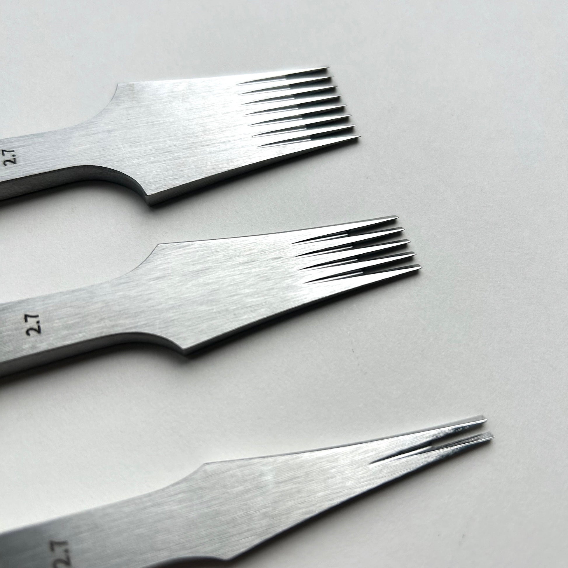 Three steel leathe pricking iron tools with textured ends on a light gray background