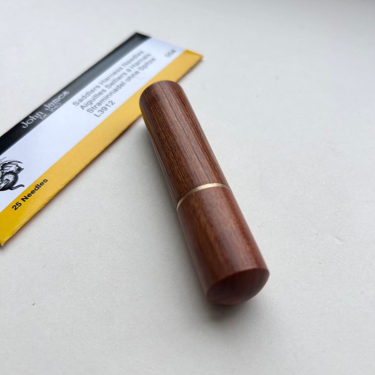 A wooden needle holder with a polished reddish-brown finish and a thin gold metal band on a light gray background.