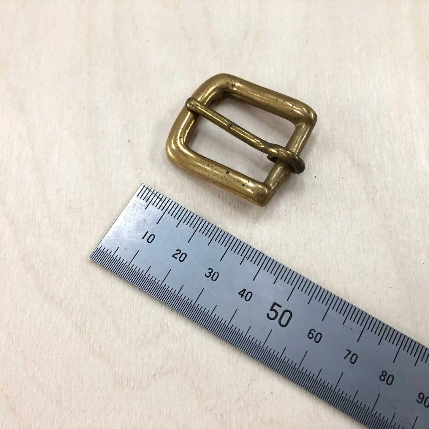 Solid brass buckle with rounded frame, featuring a pin style; ruler indicates various sizes.
