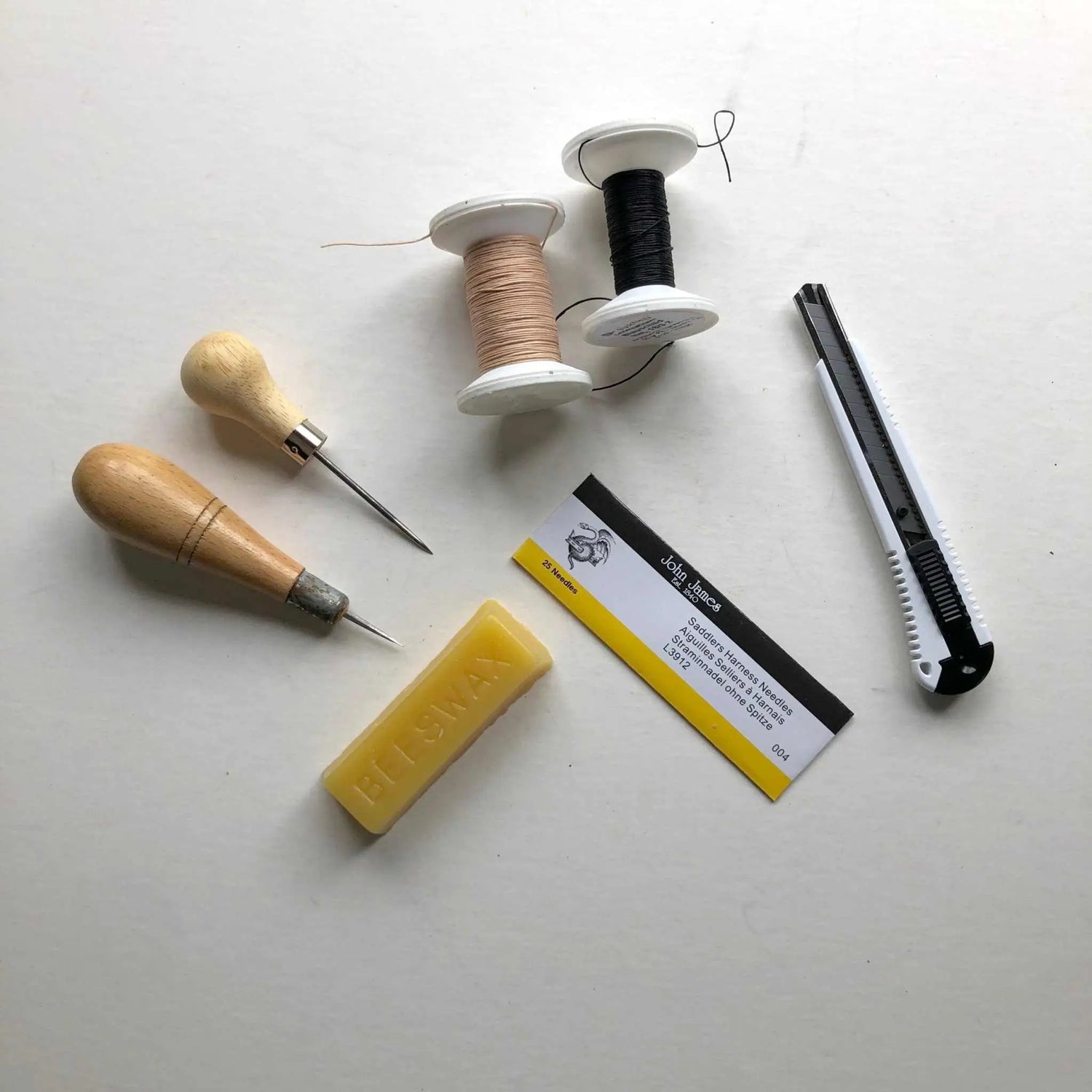 A set of leathercraft tools including awls, a knife, saddler's harness needles and a wax block