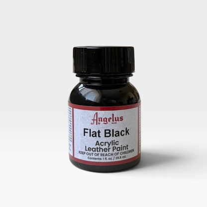 A small bottle of Angelus Flat Black acrylic leather paint, featuring a black cap and a white label with red borders, set against a plain light gray background.