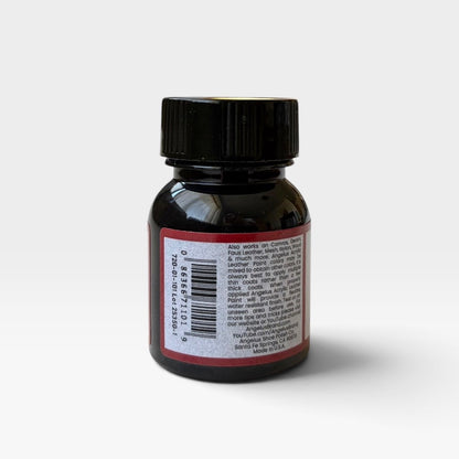 The back of a small bottle of Angelus Flat Black acrylic leather paint, featuring a black cap and a white label with red borders, set against a plain light gray background.